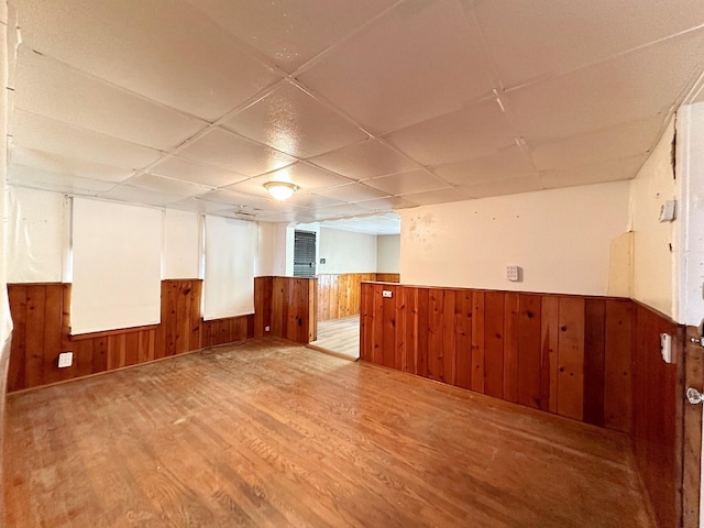 interior space with a drop ceiling, light hardwood / wood-style flooring, and wooden walls