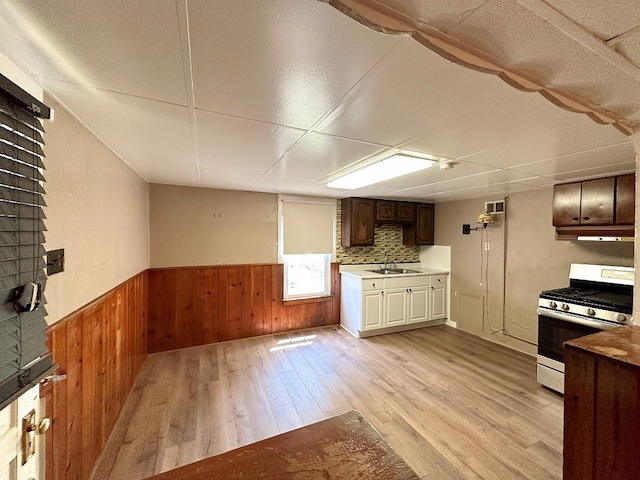 kitchen featuring range with gas stovetop, light hardwood / wood-style flooring, backsplash, sink, and wood walls