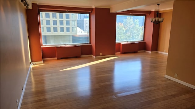 unfurnished room with a notable chandelier, ornamental molding, radiator, and light wood-type flooring