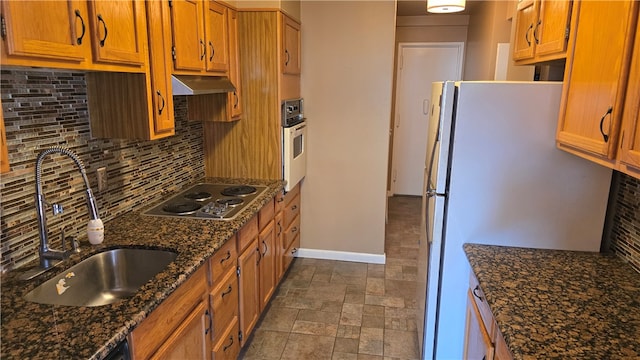 kitchen featuring oven, stainless steel gas cooktop, backsplash, dark stone counters, and white fridge