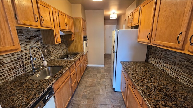 kitchen featuring dark stone countertops, sink, backsplash, and white appliances