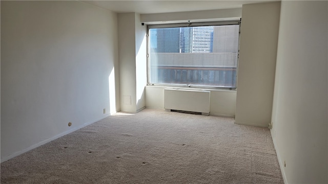 spare room featuring radiator heating unit and light colored carpet