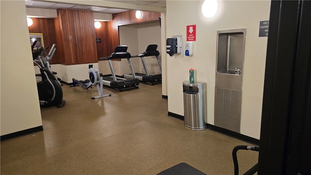 workout area featuring wood walls and a drop ceiling