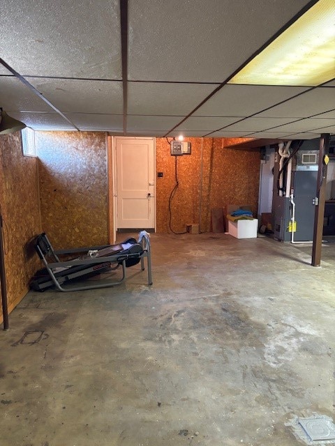 basement with a paneled ceiling and heating unit