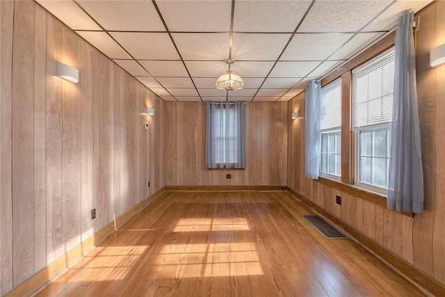 empty room featuring wooden walls, light hardwood / wood-style flooring, and a paneled ceiling