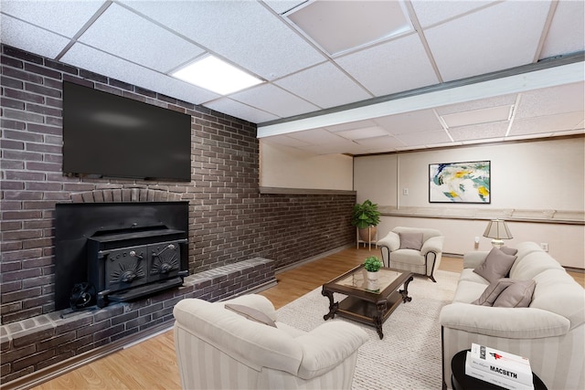 living room featuring a wood stove, light hardwood / wood-style flooring, a paneled ceiling, and brick wall