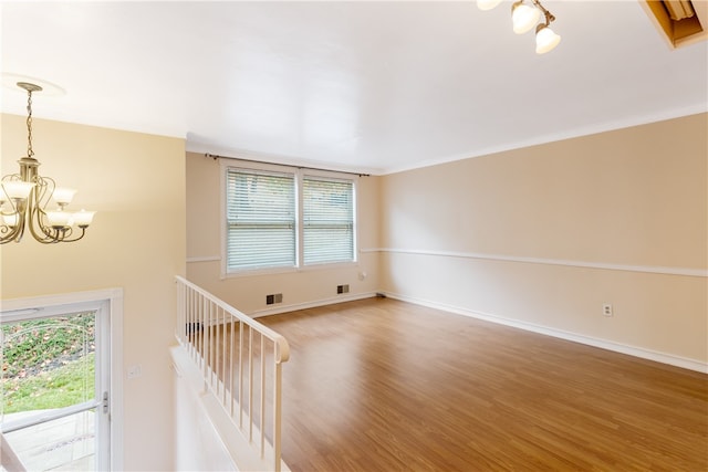 empty room with hardwood / wood-style flooring, crown molding, and a notable chandelier