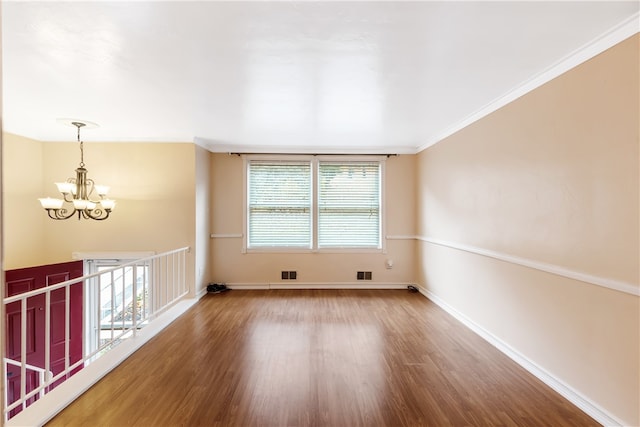 empty room with hardwood / wood-style floors, an inviting chandelier, and crown molding