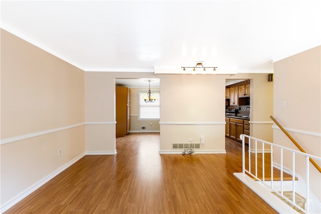 spare room with an inviting chandelier, crown molding, and light hardwood / wood-style flooring