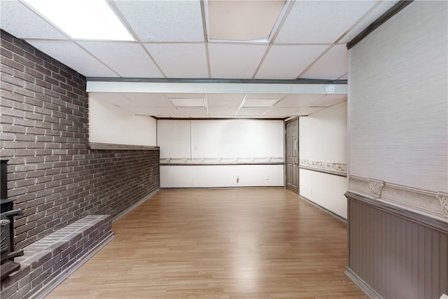 basement with brick wall, light hardwood / wood-style flooring, and a drop ceiling