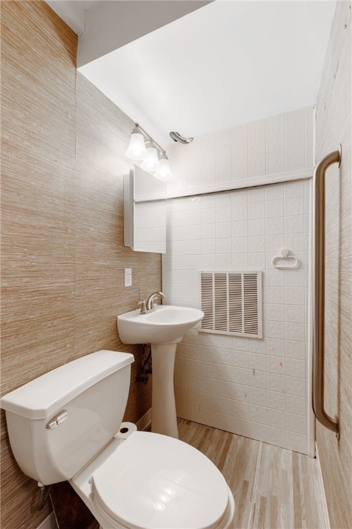 bathroom featuring hardwood / wood-style flooring, toilet, and tile walls