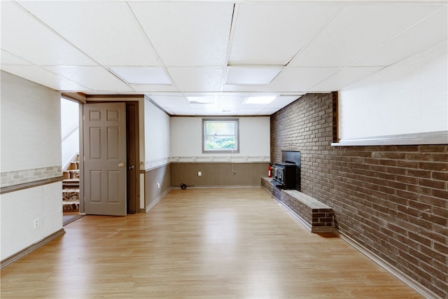 unfurnished living room with a drop ceiling, light wood-type flooring, and brick wall