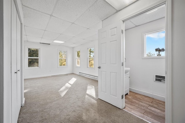 empty room with a drop ceiling, light hardwood / wood-style flooring, a baseboard heating unit, and a healthy amount of sunlight