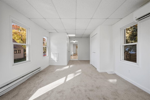 empty room featuring a baseboard radiator, a drop ceiling, a wall mounted air conditioner, and light colored carpet