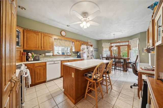 kitchen featuring white appliances, a kitchen island, a kitchen breakfast bar, ceiling fan, and light tile patterned floors