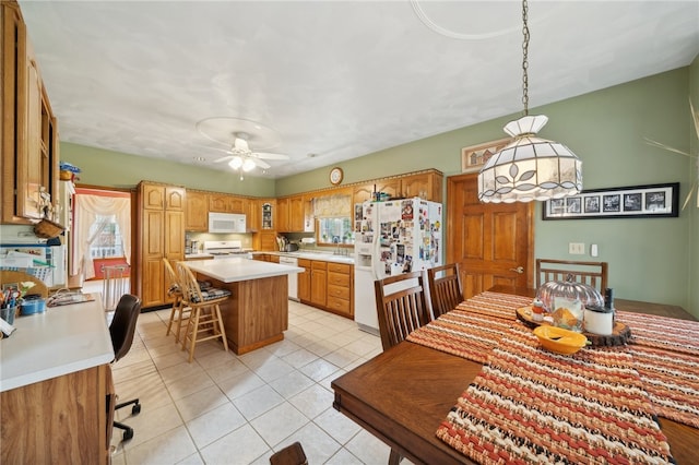 kitchen featuring white appliances, light tile patterned floors, a center island, ceiling fan, and a breakfast bar area