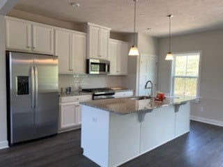 kitchen featuring stainless steel appliances, pendant lighting, a center island with sink, and white cabinets