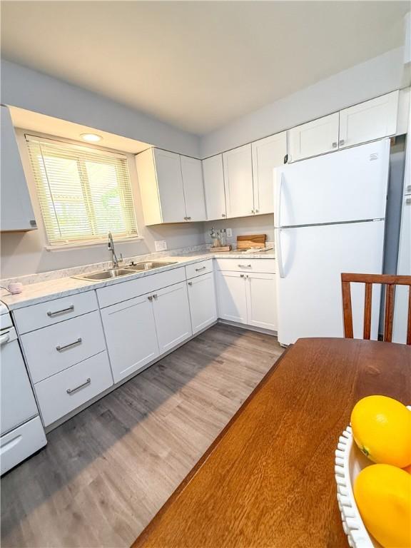 kitchen featuring freestanding refrigerator, a sink, white cabinets, wood finished floors, and stove