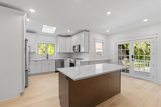 kitchen with light wood-type flooring, stainless steel appliances, white cabinets, light stone counters, and decorative backsplash