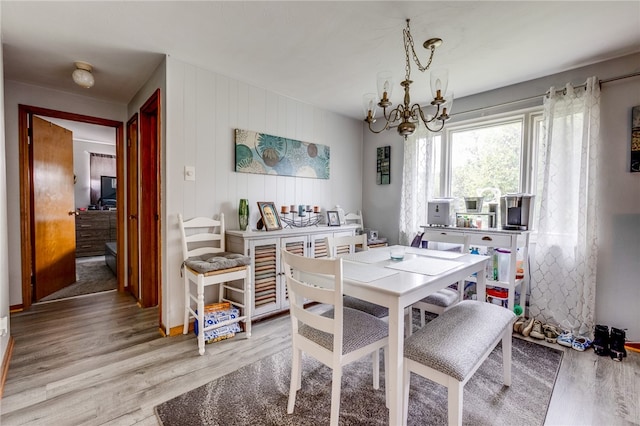 dining space with hardwood / wood-style flooring, an inviting chandelier, and wooden walls