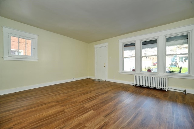 spare room with radiator, a healthy amount of sunlight, and dark wood-type flooring