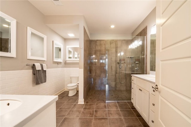 bathroom with vanity, tile patterned floors, toilet, tiled shower, and tile walls