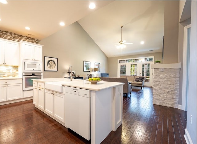 kitchen with decorative backsplash, white appliances, a center island with sink, white cabinets, and dark hardwood / wood-style floors