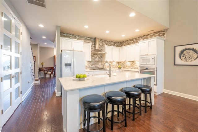 kitchen featuring appliances with stainless steel finishes, dark hardwood / wood-style flooring, wall chimney exhaust hood, white cabinets, and an island with sink