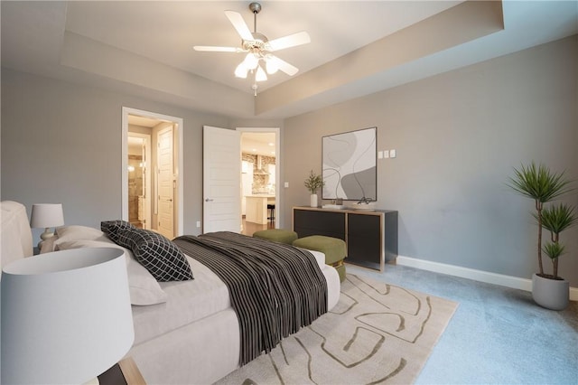 carpeted bedroom featuring ceiling fan, a raised ceiling, and ensuite bath