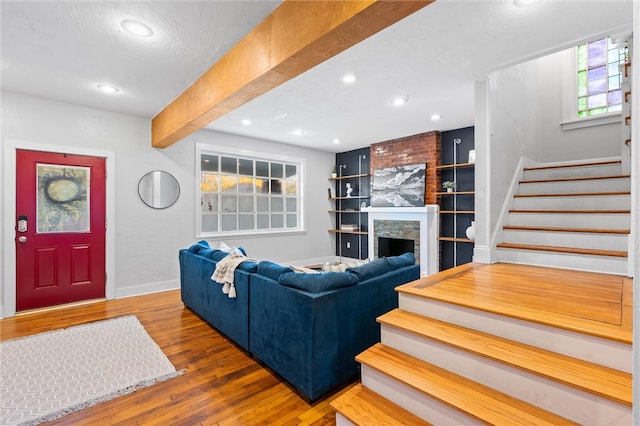 living room featuring a stone fireplace, a textured ceiling, hardwood / wood-style flooring, and beamed ceiling