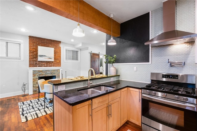 kitchen featuring sink, a barn door, dark hardwood / wood-style flooring, wall chimney exhaust hood, and stainless steel gas range oven