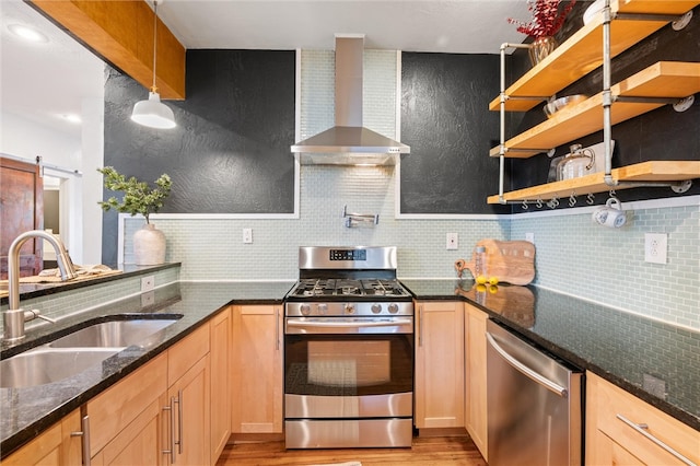 kitchen featuring wall chimney range hood, light hardwood / wood-style flooring, sink, a barn door, and appliances with stainless steel finishes