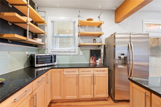 kitchen with appliances with stainless steel finishes, light hardwood / wood-style flooring, dark stone countertops, and backsplash