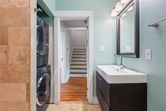 clothes washing area with sink, stacked washer and clothes dryer, and light tile patterned floors