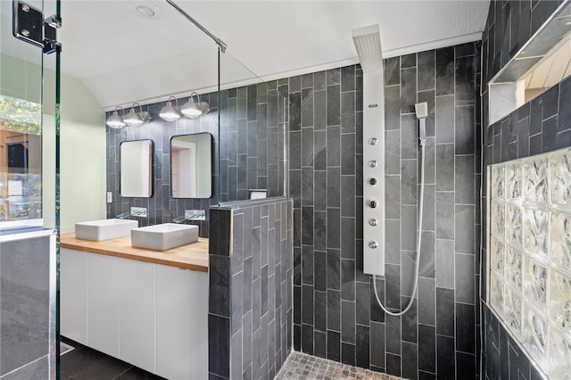 bathroom featuring tile walls, vaulted ceiling, tiled shower, vanity, and tile patterned floors