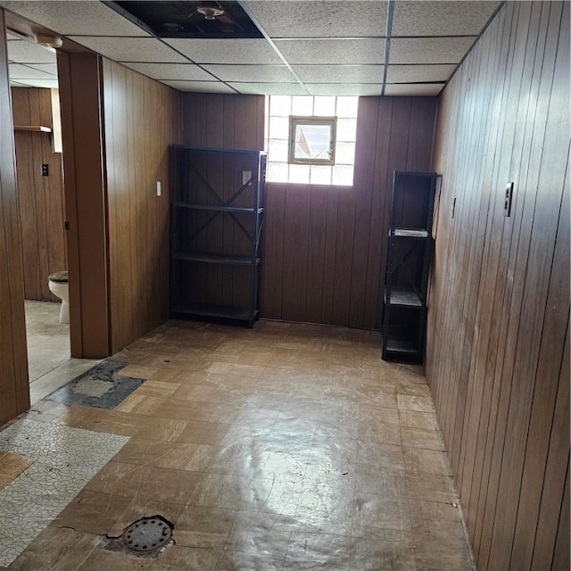 basement with a drop ceiling and wooden walls