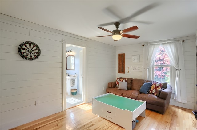 living room with wood walls, light wood-type flooring, and ceiling fan