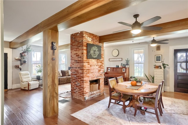 dining room with ceiling fan, hardwood / wood-style flooring, beam ceiling, and a fireplace