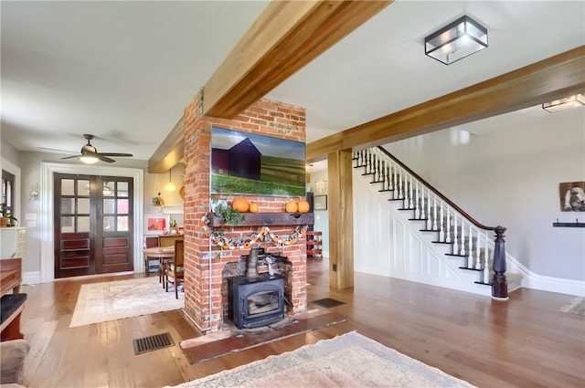 living room featuring beam ceiling, hardwood / wood-style flooring, a wood stove, and ceiling fan