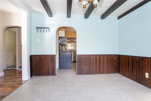 unfurnished room featuring beamed ceiling, wooden walls, and light wood-type flooring