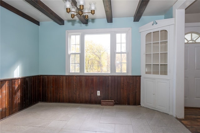 unfurnished dining area with beam ceiling, wood walls, an inviting chandelier, and light tile patterned floors