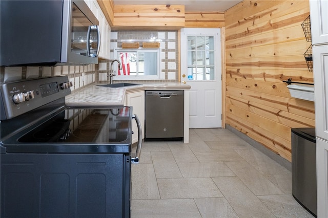 kitchen with wood walls, stainless steel appliances, sink, white cabinetry, and tasteful backsplash