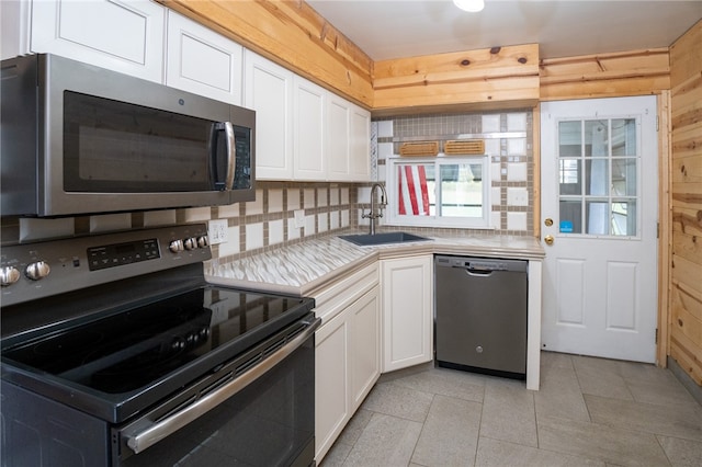 kitchen with tasteful backsplash, white cabinetry, sink, wooden walls, and stainless steel appliances