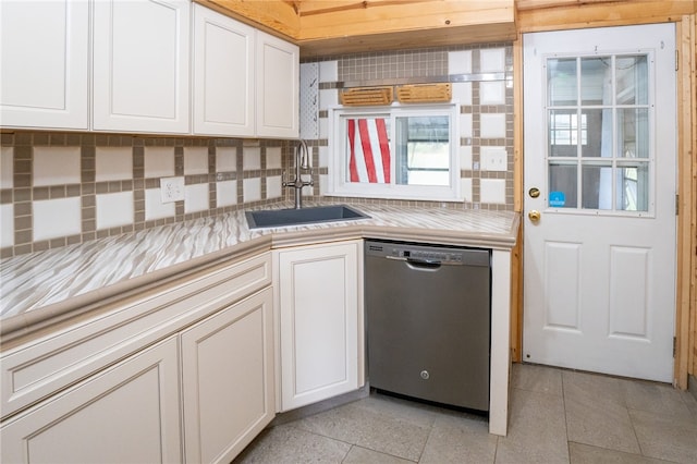 kitchen featuring sink, light tile patterned floors, stainless steel dishwasher, white cabinetry, and tasteful backsplash