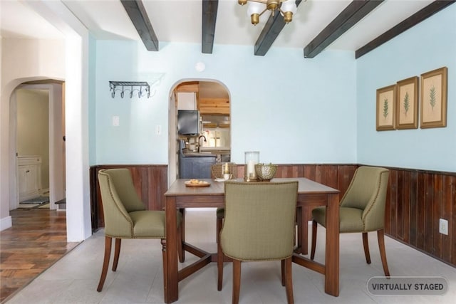 dining area featuring beamed ceiling, wooden walls, and light hardwood / wood-style floors