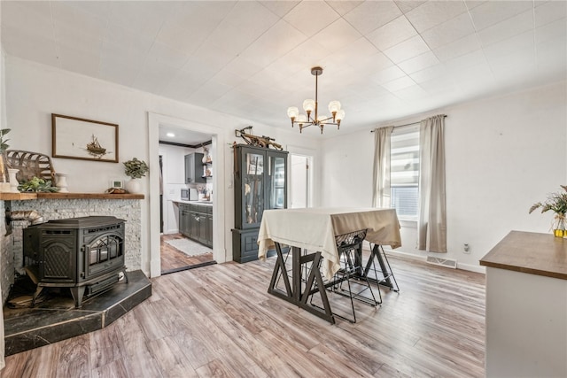 dining space with light hardwood / wood-style floors, a wood stove, and an inviting chandelier