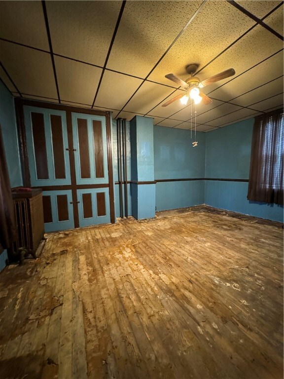 empty room with a paneled ceiling, wood-type flooring, and ceiling fan