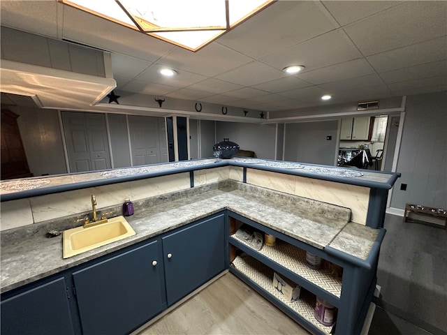 kitchen featuring wood-type flooring, sink, a drop ceiling, and blue cabinets