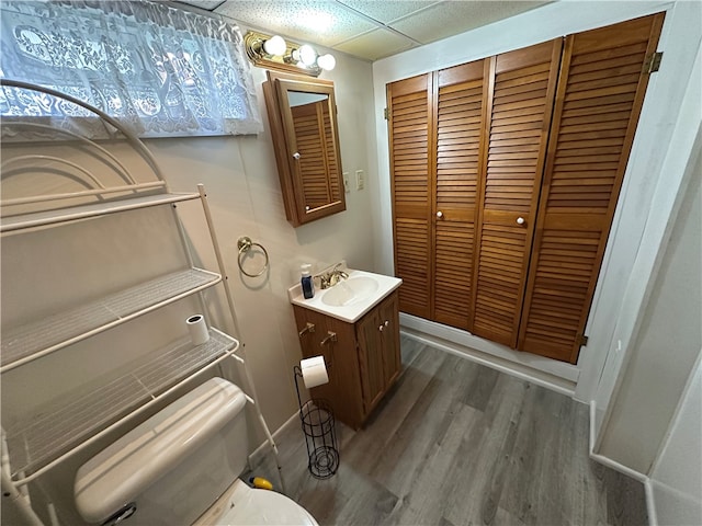 bathroom with toilet, a drop ceiling, hardwood / wood-style flooring, and vanity