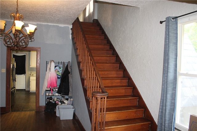 stairway with an inviting chandelier, a textured ceiling, and wood-type flooring